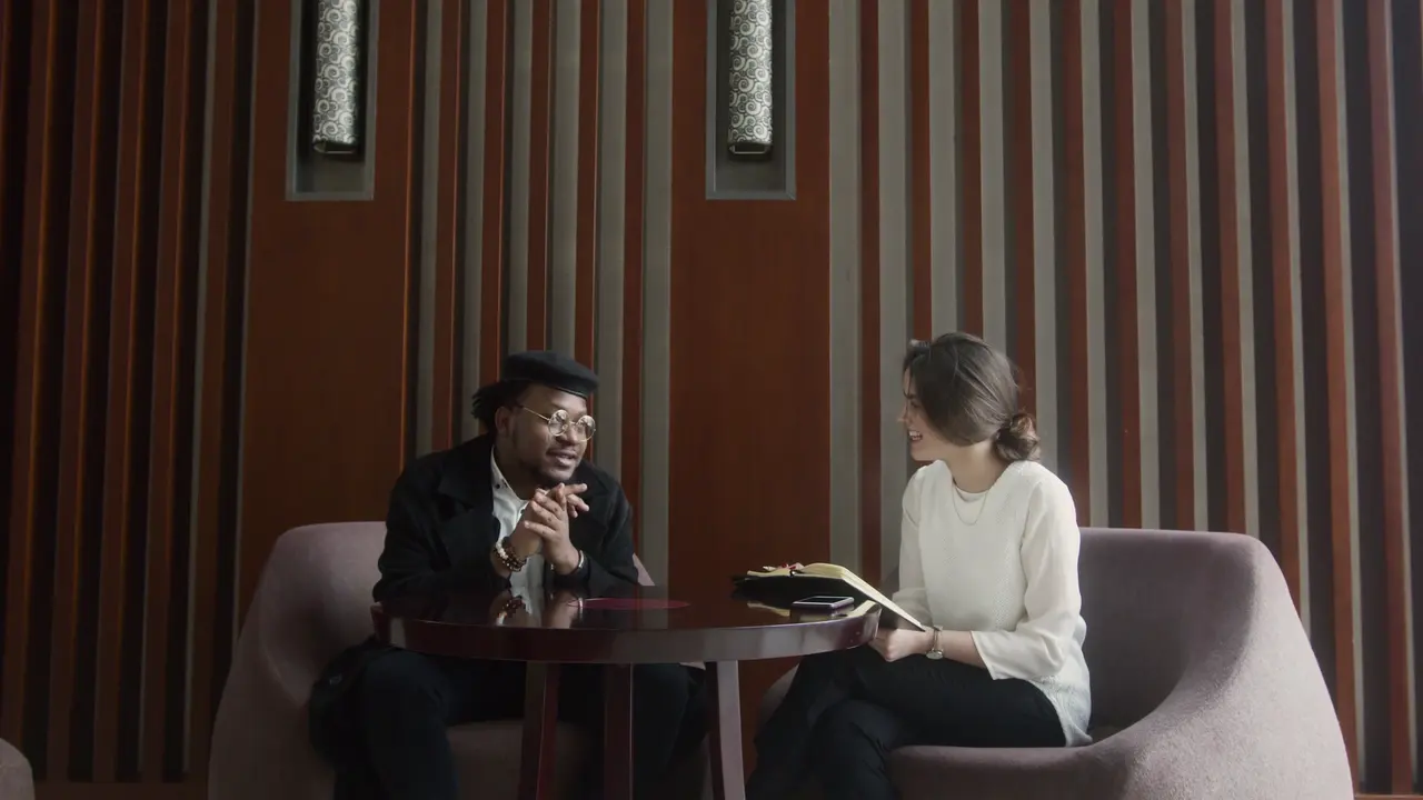 Two people talking at a small table, each in a window of their own, the one speaking marked